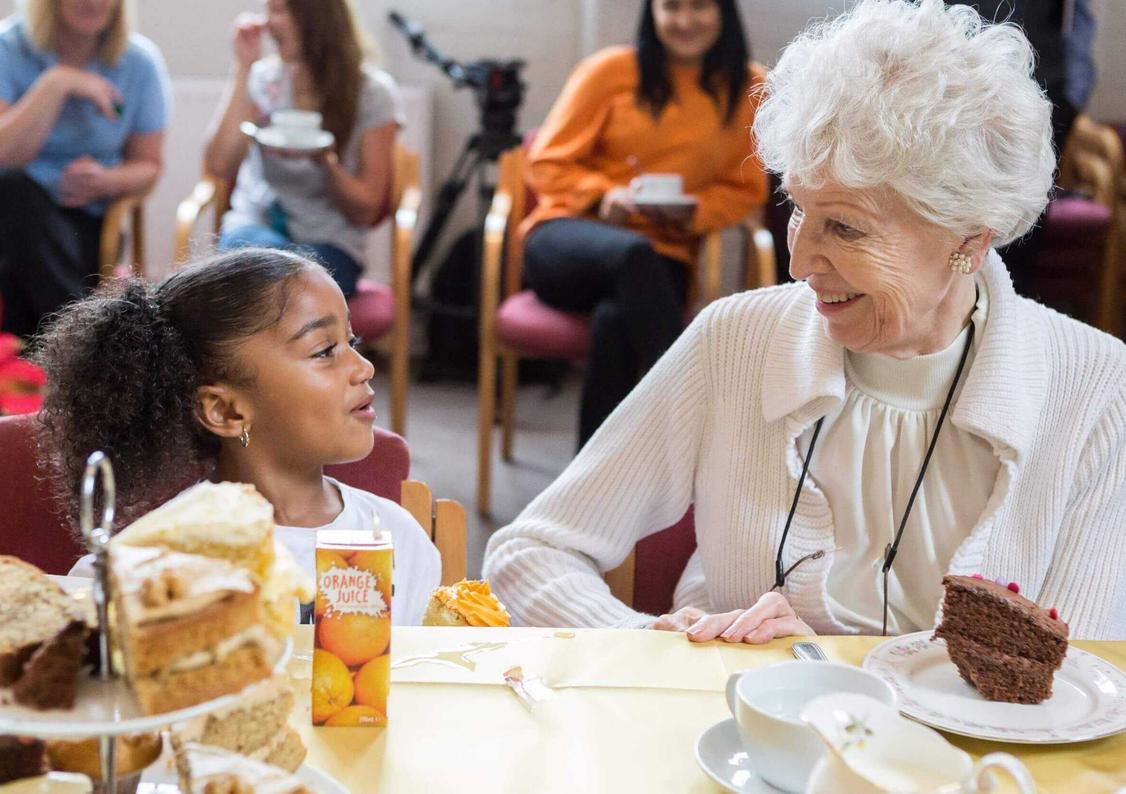 A small child having cake with an elderly lady
